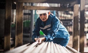 Woman with hard hat loading long pipes in construction area