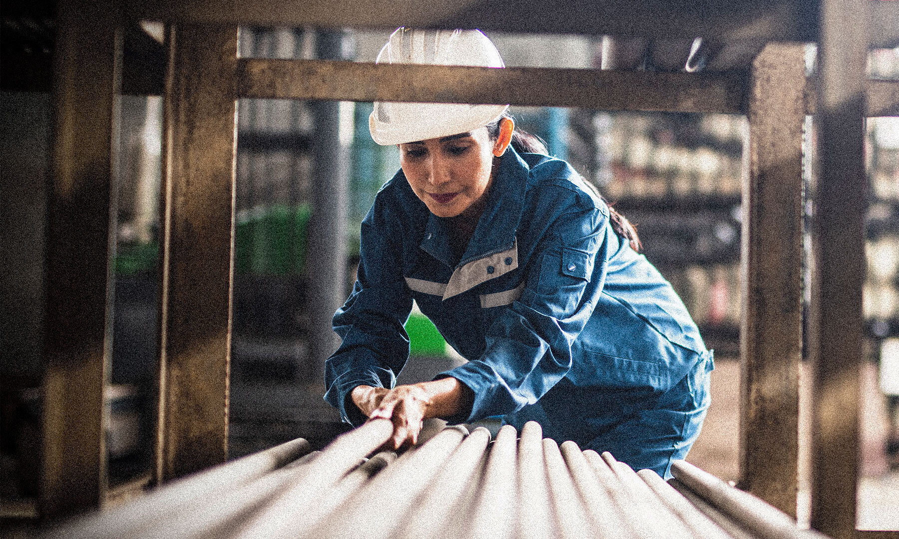 Woman with hard hat loading long pipes in construction area