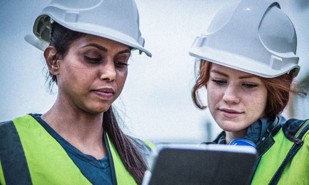 Two women in hard hats working and review a document