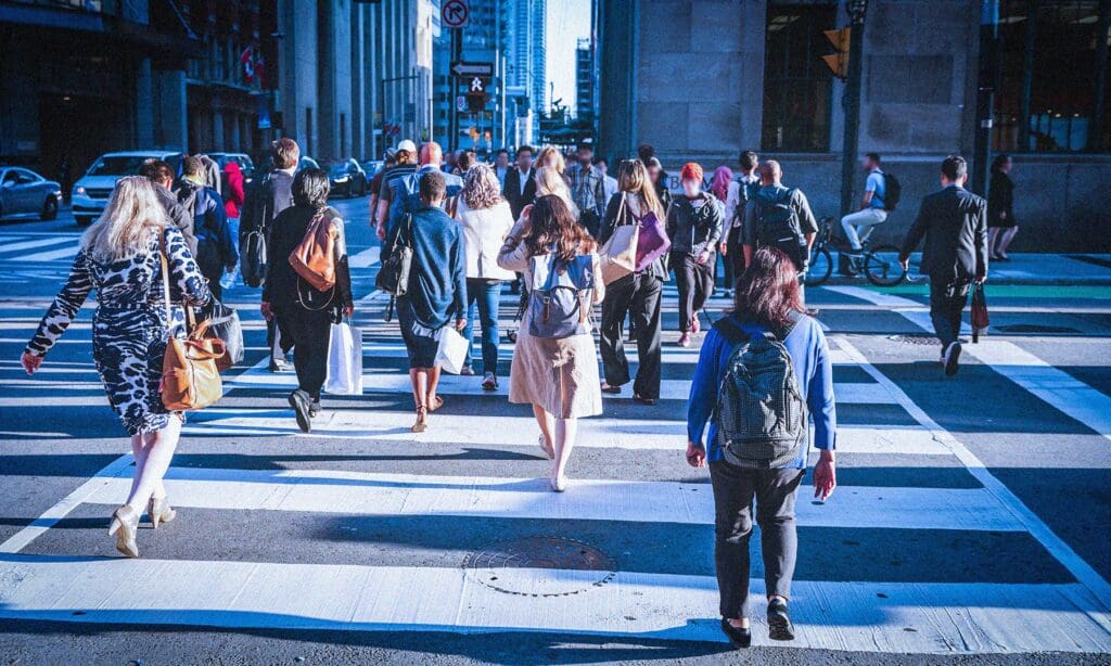 Many people walking across a cross walk in a busy city