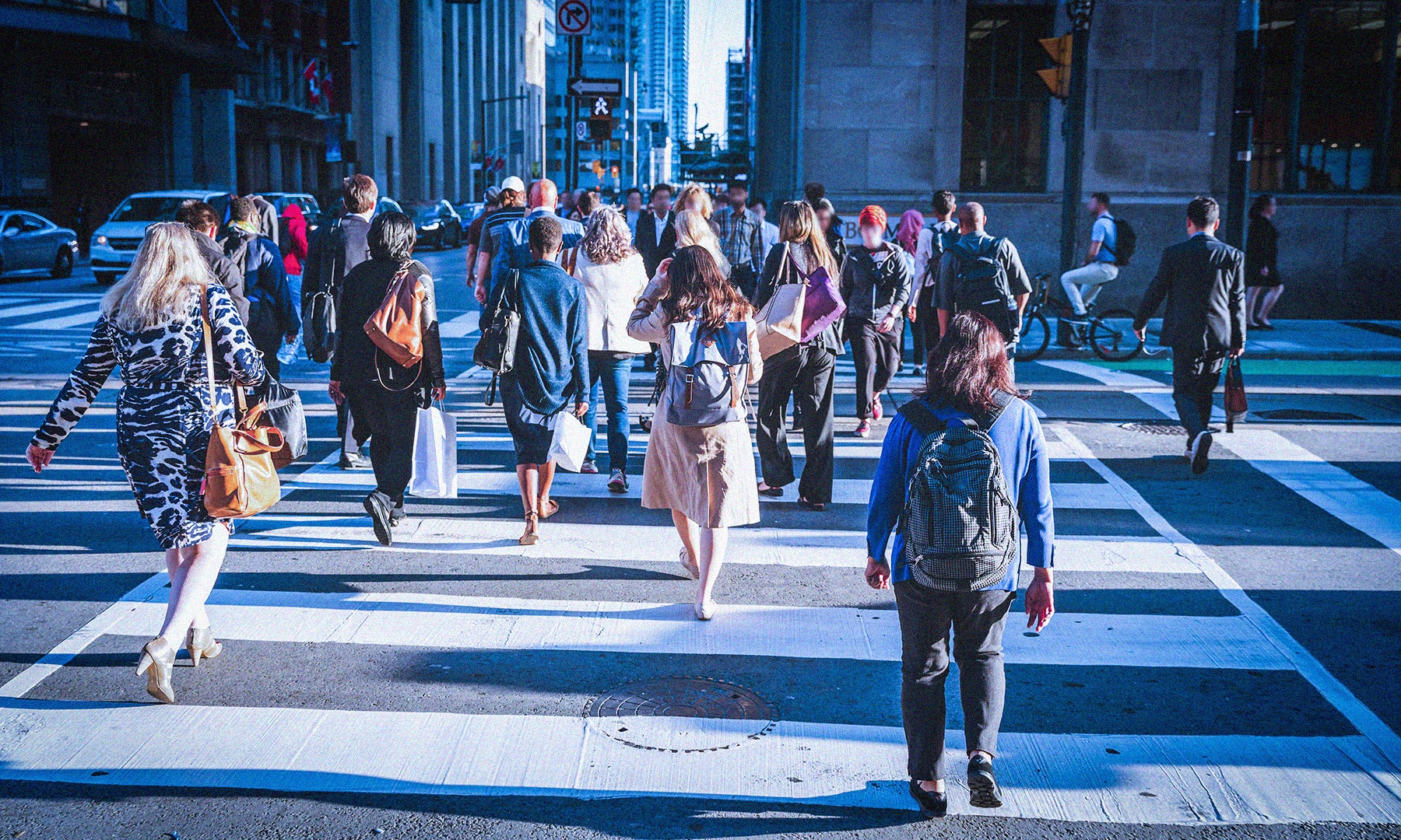 Many people walking across a cross walk in a busy city
