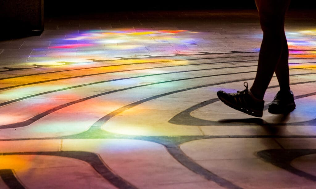 Feet in sneakers, one foot stepping forward on a floor lit up in different colours