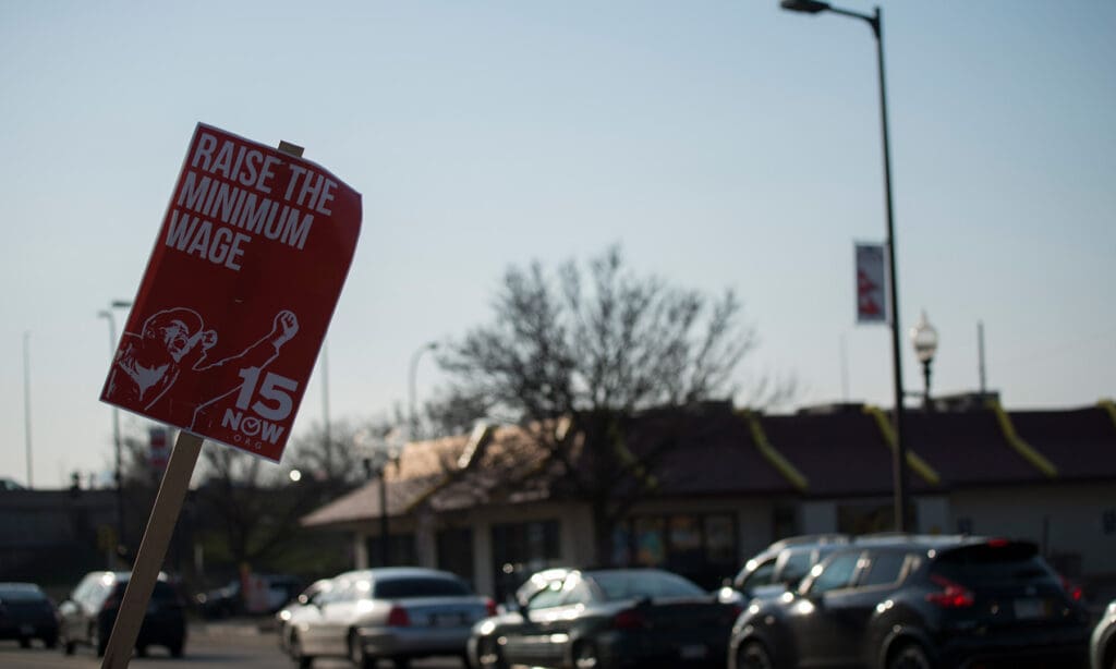 Minimum wage protest sign in red. text says "Minimum wage now"