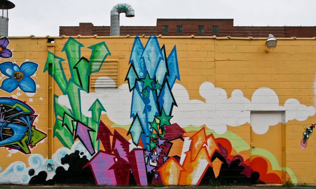 Different colour arrows graffitied on a mustard colour wall. Green arrows, blue, purple and yellow arrows.