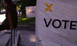 White sign with yellow X and a black letters stating"Vote"