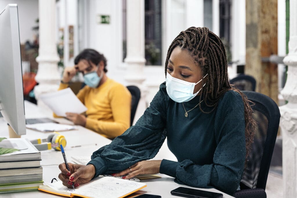 woman in office writing with a mask