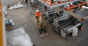 Worker in orange coat pushing forklift in factory