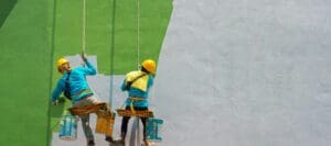 Two workers painting an exterior wall of a building, hanging with harnesses.