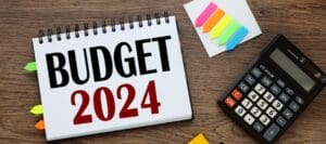 "Budget 2024" written on a coiled paper pad on a desk.