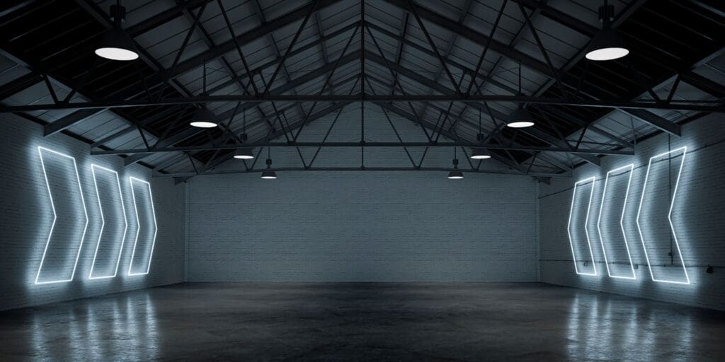 Empty large warehouse interior with cement floor, illuminated by white arrow shaped neon lights from side brick walls. A large blank brick wall background with copy space in the center. 3D rendered image.