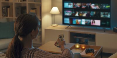 Woman relaxing on the couch, she is using the remote control and choosing a TV show or movie on the television menu