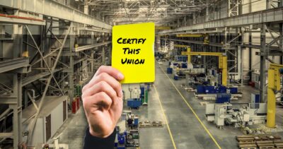 Factory in background with a hand holding a yellow card that says certify this unon