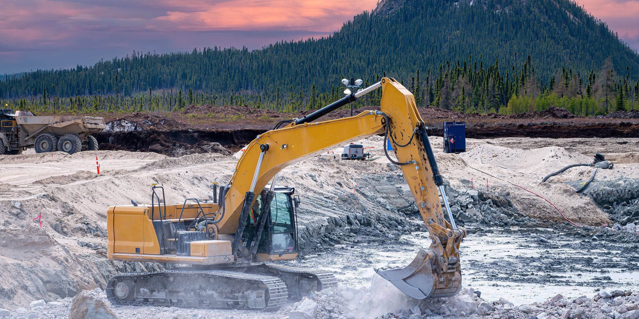 Yellow excavator working on a construction site in the taiga at sunset